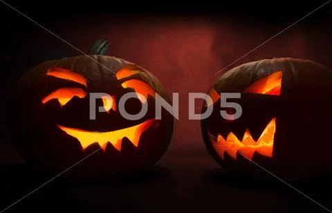 Two Carved Faces Of Pumpkins Glowing On Halloween On Red Background
