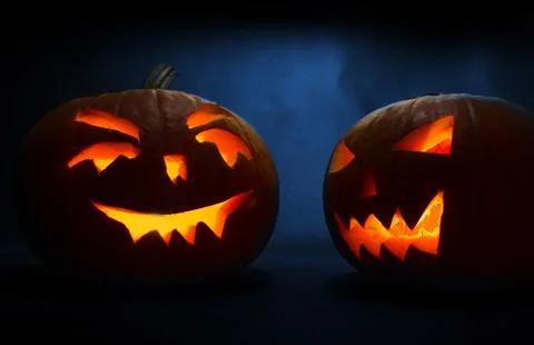 Two carved faces of pumpkins glowing on Halloween on blue background Stock Photos