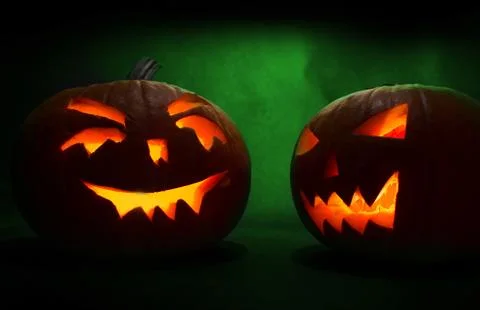 Two carved faces of pumpkins glowing on Halloween on green background 写真素材