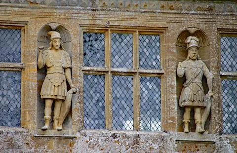 Two carved figures stand either side of leaded windows at an English country Stock-Fotos