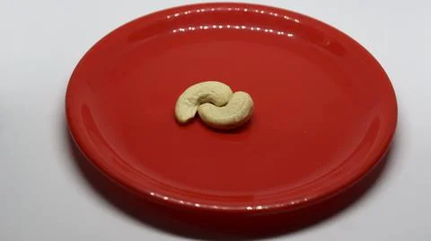 Two cashew nuts is on a white background on a red plate Stock Photos