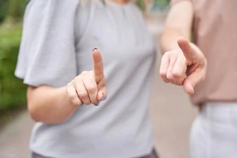 Two caucasian adults gesturing with pointing fingers in casual attire outd... Stock Photos
