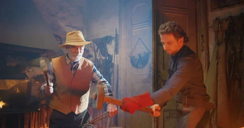 Two Caucasian blacksmiths, young and old men, working in antique forge and Stock Footage 135330983
