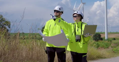 Two Caucasian engineer in bright safety jacket discussing blueprint near wind Stock Footage 337161833