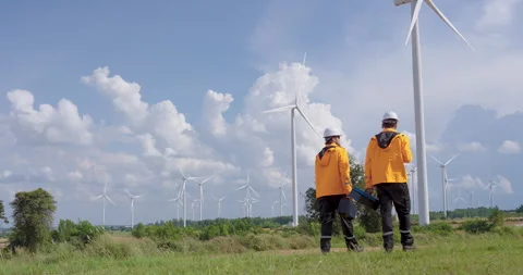 Two caucasian engineer walking in wind farm field with toolboxes, teamwork for Stock Footage 325844545