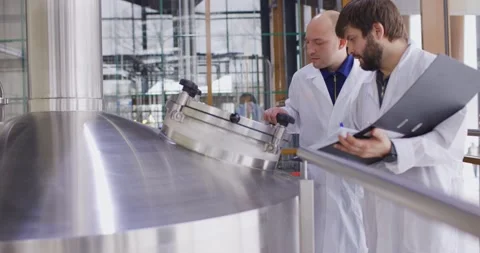 Two Caucasian mans working at a brewery factory. A male brewer checks the Stock Footage 147950536