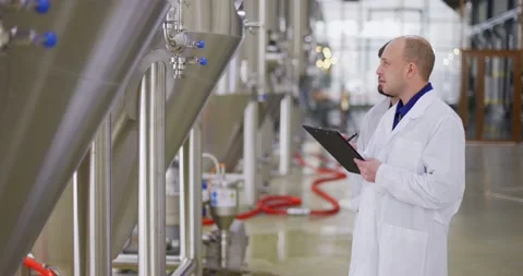 Two Caucasian mans working at a brewery factory. A male brewer checks the Stock Footage 148229947