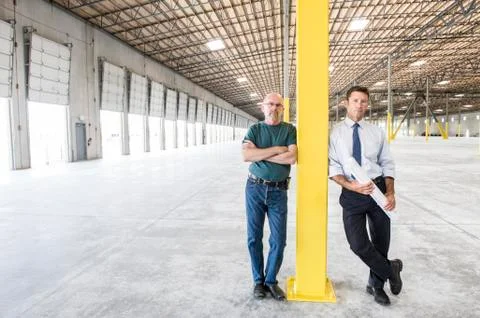 Two caucasian men standing in front of loading dock doors in a new warhouse Stock Photos