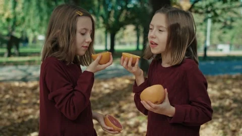 Two caucasian sisters eating oranges and grapefruit in the autumn Stock Footage 219925713
