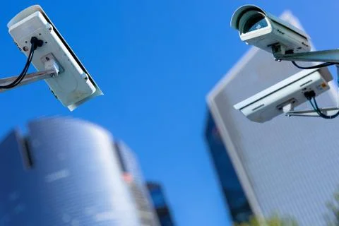 Two cctv security camera in a city with blury business building on background Foto stock