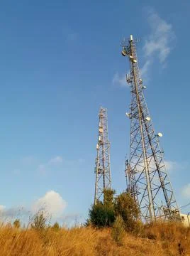 Two cell towers on a background of dry grass and blue sky Stock Photos