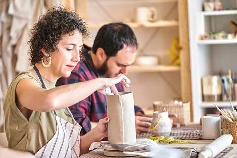 Two ceramic artists work intensively on ceramic pieces at a studio 스톡 사진