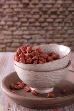 Two ceramic bowls full of peanuts coated by sweet red dough Stock Photos