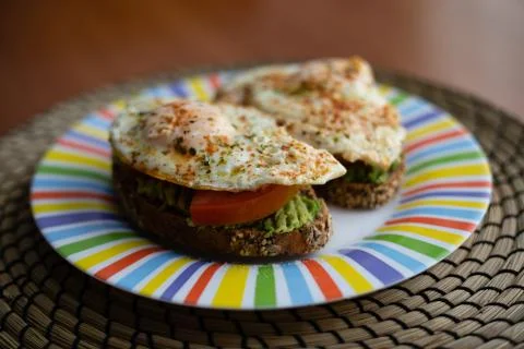 Two cereal bread slices with avocado, tomato and fried egg on top, presented  Stock Photos