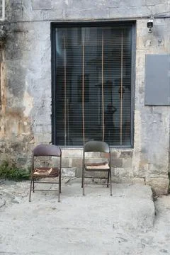 Two chairs in front of an old building with black blinds, stone floor, phot.. Stock Photos