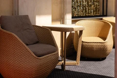 Two chairs made of woven material sit next to a small table in a bright cor.. Stock Photos
