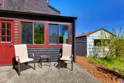 Two chairs next to red door and small black house. Stock Photos