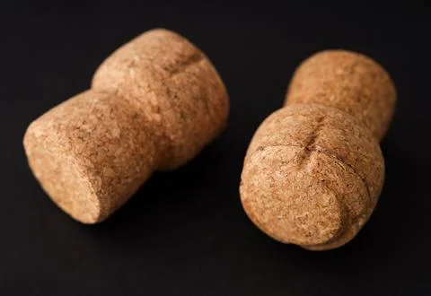 Two champagne corks lying on a black background. Stock Photos