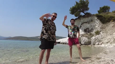 Two charismatic young men waving hand on the beach with unique nature scenery. Stock Footage 219935420