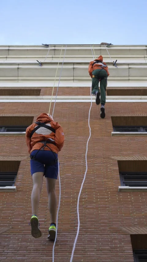 Two Charity Fundraisers Abseiling Down a High-Rise Brick Building Side by Side. Stock Footage 340023853