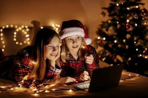 Two charming sisters lie on the bed with a laptop on Christmas or New Year's eve Stock Photos