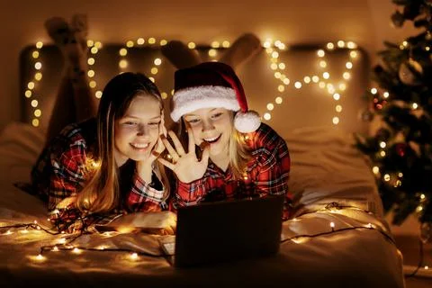 Two charming sisters lie on the bed with a laptop on Christmas or New Year's eve Stock Photos