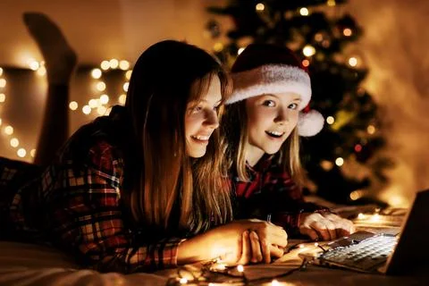 Two charming sisters lie on the bed with a laptop on Christmas or New Year's eve Stock Photos