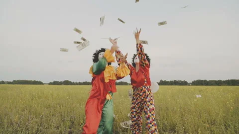 Two cheerful clowns catch falling dollars in the field. Video stock 92183099