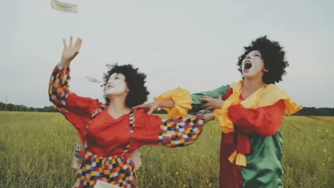 Two cheerful clowns catch falling dollars and fight in the field. Video stock 92183148