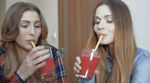 Two cheerful girls drinking fruit cocktail and gossiping. Stockbeeldmateriaal 62767518