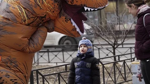 Two cheerful kids talking to person in dinosaur costume at sidewalk Stock Footage 84930845