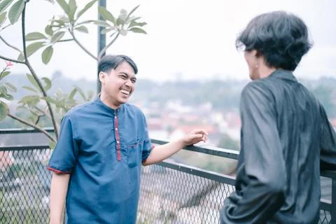 Two cheerful men engaging in friendly conversation on rooftop terrace Foto stock