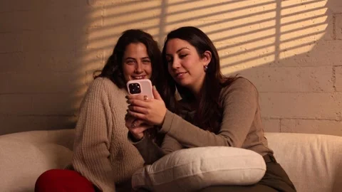 Two cheerful women using smartphone on sofa Stock Footage 331666003