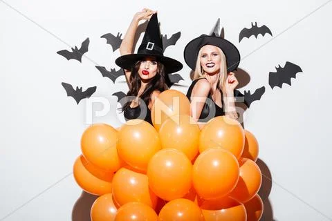 Two cheerful women in witch costumes dancing with orange balloons Stock Photos