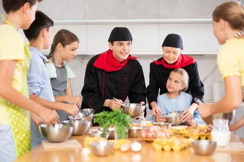 Two chefs teach children how to cook food - they beat eggs with whisk Stock Photos