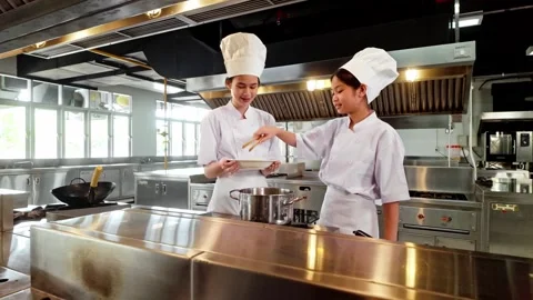 Two chefs in white uniforms and hats collaborate while cooking on a stove 動画素材 327122876