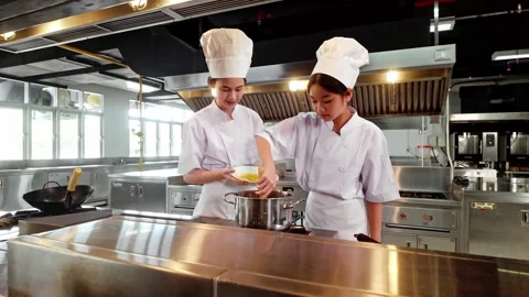 Two chefs in white uniforms and hats collaborate while cooking on a stove 動画素材 328076871