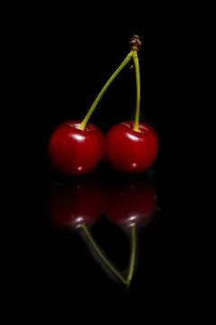 Two cherries on a black background with reflection. Stock Photos