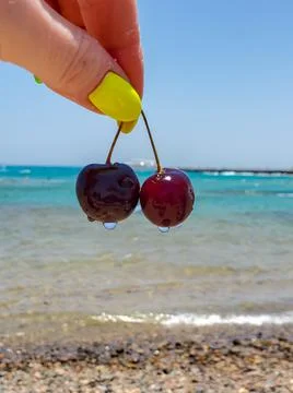 Two cherries in a woman's hand close-up on the background of the sea Stock Photos