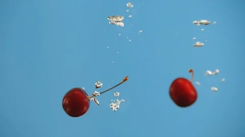 Two cherry berries cherries fall into water on blue background slow motion Video stock 91014577