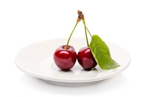 Two Cherry berries with green leaf  on a white plate isolated on a white back Stock Photos