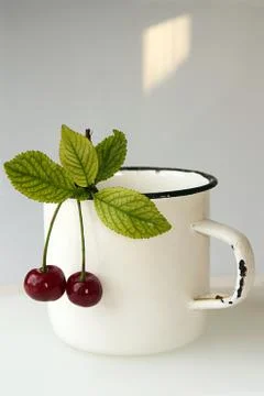 Two cherry with leaves hanging on white mug Stock Photos