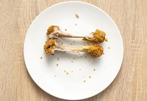 Two chicken bones as left over on white plate. Unhealthy fast food, chicken Stock Photos