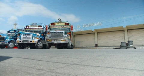Two Chicken busses driving close in Xela with stationary bus and Guatemala sign 動画素材 125791262