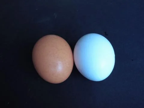 Two chicken eggs on a black background. White and red egg on the table. Stock Photos