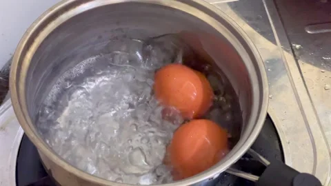Two chicken eggs boiling in a stainless steel pot with hot bubbling water Stock Footage 327228338