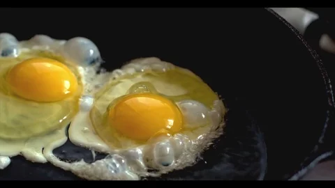 Two chicken eggs fried in a black frying pan on a gas stove Stock Footage 70643780