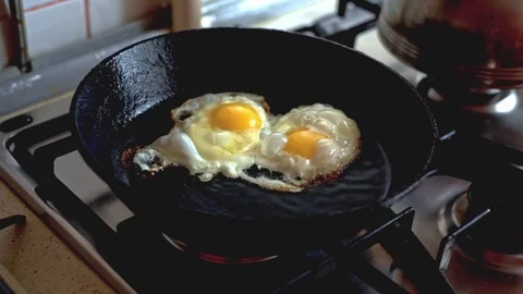 Two chicken eggs fried in a black frying pan on a gas stove Stock Footage 70643787