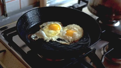 Two chicken eggs fried in a black frying pan on a gas stove Stock Footage 70643900