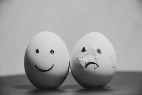 Two chicken eggs, one with joy, and the second broken with sad emotions on .. Stock Photos